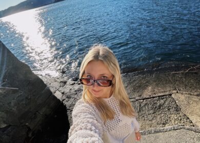 Blonde woman in sunglasses standing by water