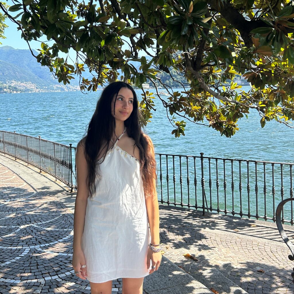 Woman in white dress standing by tree and blue water