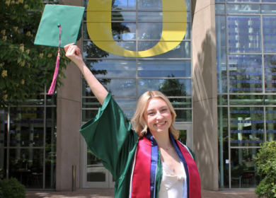 Woman on University of Oregon campus in graduation gown and cap